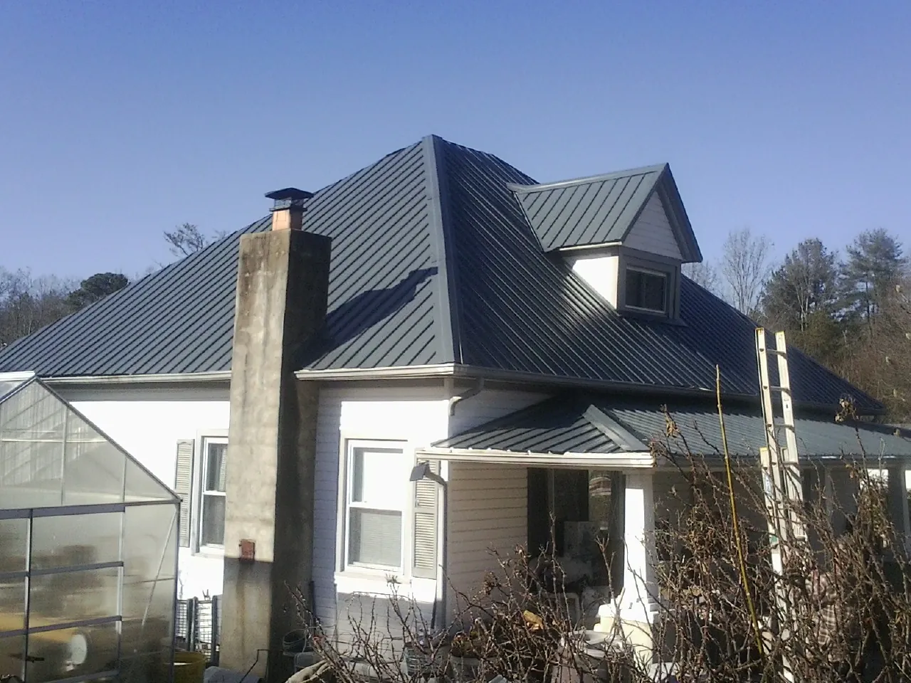Dark blue standing seam metal roof on a white farmhouse with dormer — Slate & Tile Roof Repair by Roofing Brothers in Rose Creek