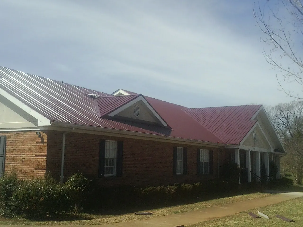 Red metal roof with gabled entries on a long brick building, from a Hail Damage Roof Repair job in Rose Creek