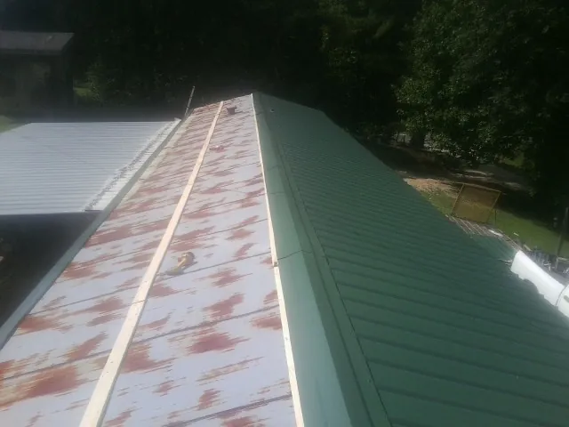 Old rusted panels beside newly installed green metal roofing in Rose Creek