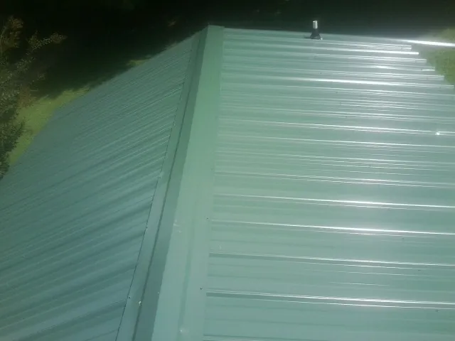 New green metal panels meeting at the ridge of a roof — Flat Roof Repair work by our crew in Rose Creek