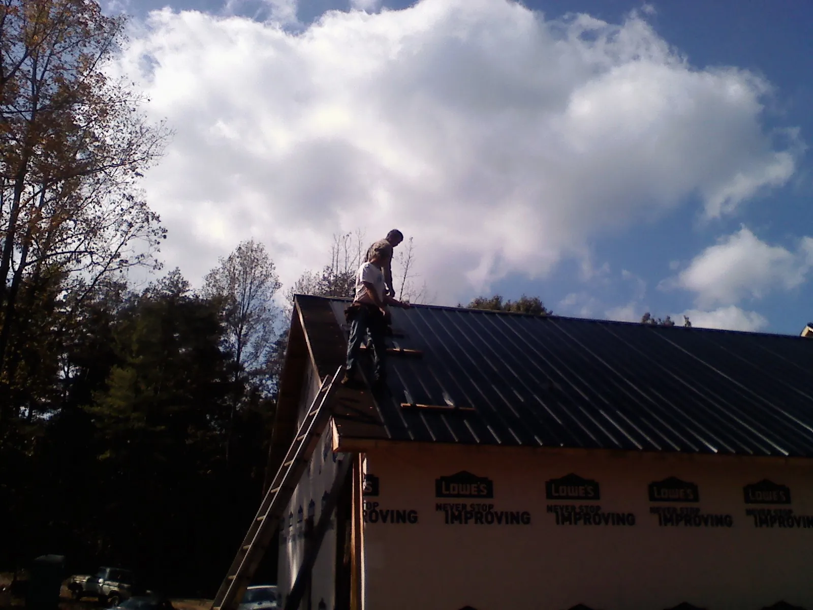 Roofer fastening dark metal panels high against a cloudy sky, from a Roof Inspection job in Rose Creek
