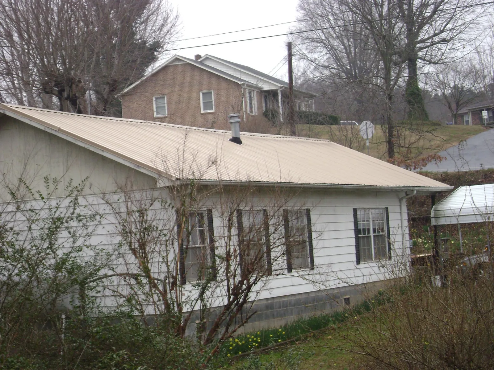 Tan metal roof on a white sided house set into a hillside — Commercial Roofing by Roofing Brothers in Rose Creek