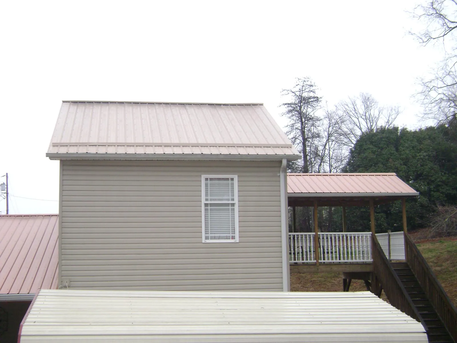 Tan metal roofs on a two story addition and attached porch, from a Roof Replacement job in Rose Creek