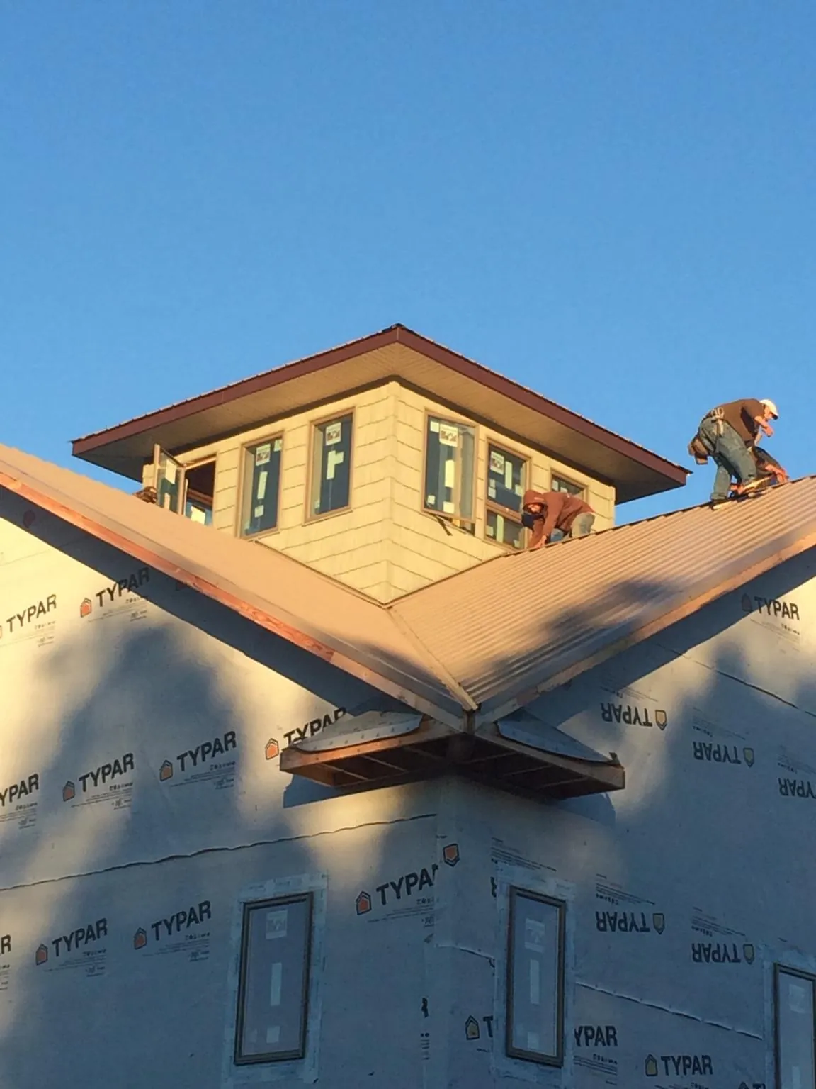 Roofers working around a rooftop cupola on a new metal roof at sunset — Roof Waterproofing in Rose Creek by Roofing Brothers